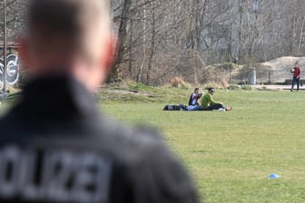 Polizist blickt auf Wiese im Park am Gleisdreieck: Berliner Polizisten kontrollieren die Einhaltung der Corona-Maßnahmen.