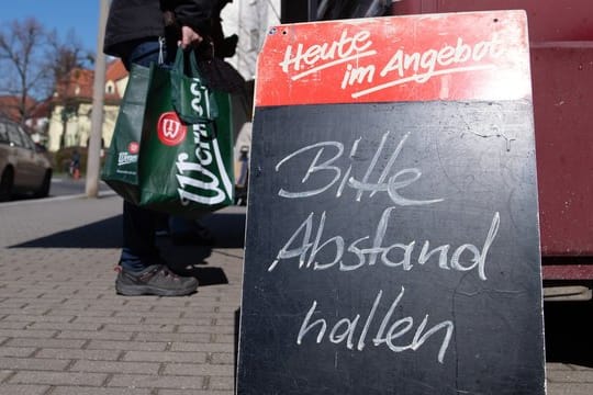 Ein Schild mit der Aufschrift "Bitte Abstand halten" auf einem Wochenmarkt.