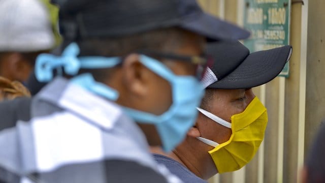 Männer mit Mundschutzmasken am Eingang des Friedhofs "Jardines de la Esperanza" in der Hafenstadt Guayaquil in Ecuador. Männer mit Mundschutzmasken am Eingang des Friedhofs "Jardines de la Esperanza" in der Hafenstadt Guayaquil in Ecuador.