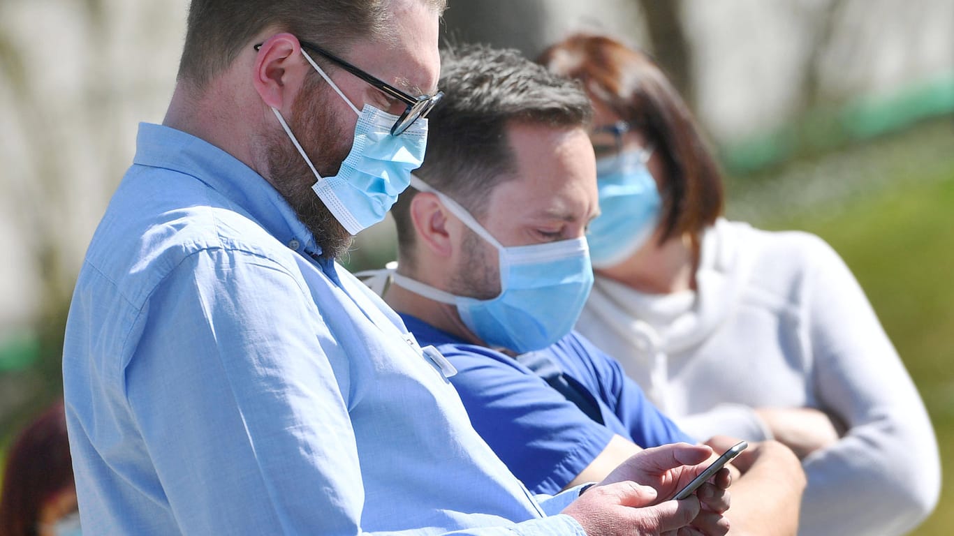 Menschen mit Mundschutz schauen auf ein Smartphone: Apps sollen helfen, die Coronavirus-Epidemie einzudämmen.