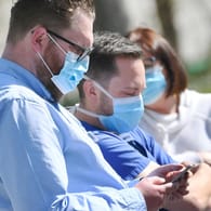 Menschen mit Mundschutz schauen auf ein Smartphone: Apps sollen helfen, die Coronavirus-Epidemie einzudämmen.
