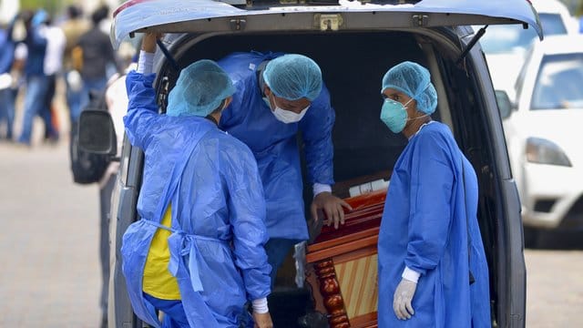 Männer mit Schutzanzügen laden in der Hafenstadt Guayaquil in Ecuador einen Sarg in einen Wagen vor einem Krankenhaus.