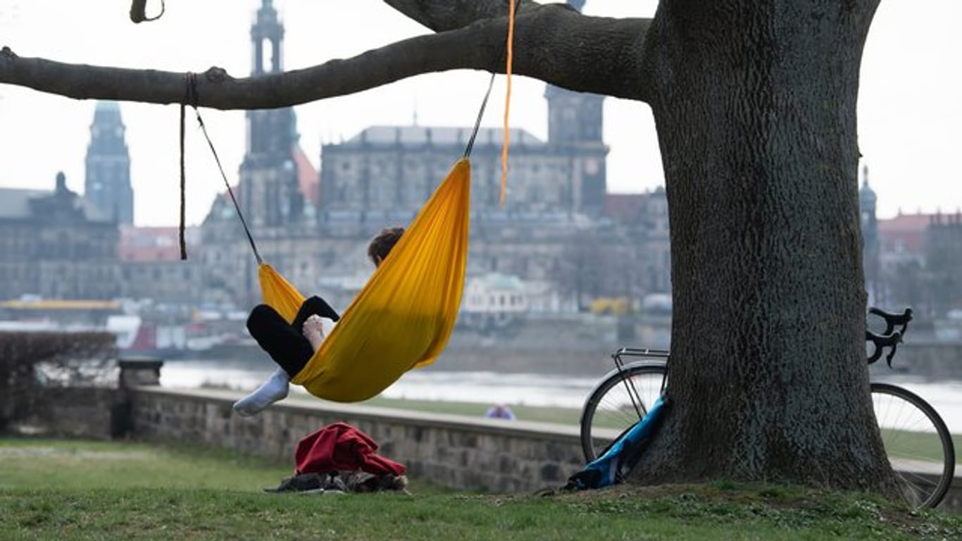 Ein Mann hat es sich am Ufer der Elbe vor der Kulisse der Dresdner Altstadt in einer Hängematte gemütlich gemacht.