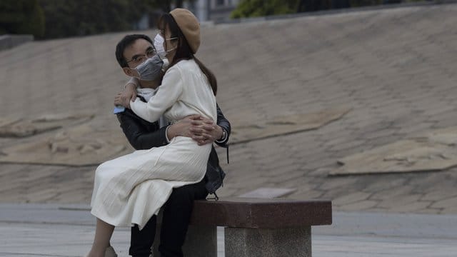 Ein Paar mit Mundschutz sitzt auf einer Bank im chinesischen Wuhan. Ein Paar mit Mundschutz sitzt auf einer Bank im chinesischen Wuhan.