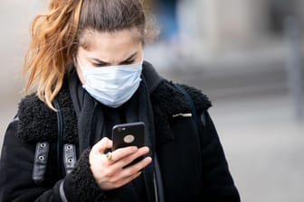 Junge Frau mit Gesichtsmaske und Smartphone: Eine datenschutzfreundliche App soll bei der Nachverfolgung von Kontakten von Covid-19-Patienten helfen.