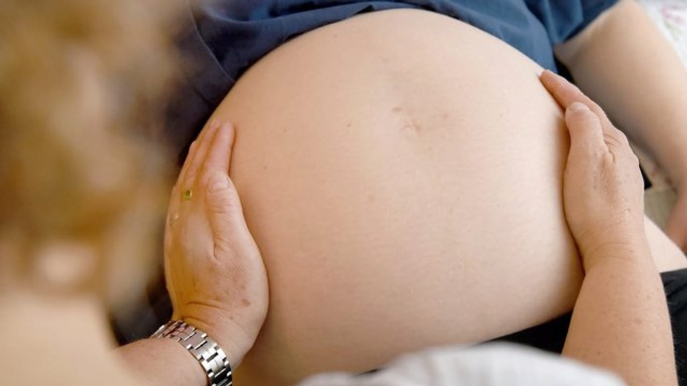 Eine Hebamme tastet den Bauch einer hochschwangeren Frau ab.