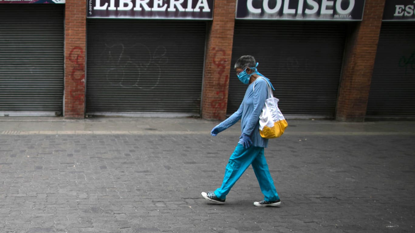 Venezuela, Caracas: Eine Frau, die eine schützende Gesichtsmaske und Einweghandschuhe trägt, geht während der Ausgangssperre an geschlossenen Läden vorbei.