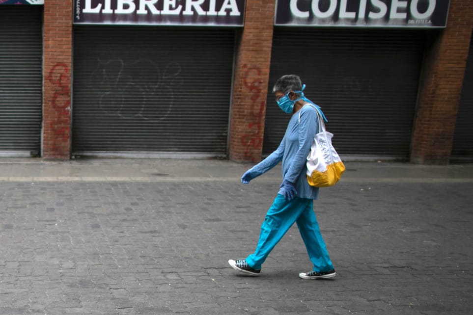 Venezuela, Caracas: Eine Frau, die eine schützende Gesichtsmaske und Einweghandschuhe trägt, geht während der Ausgangssperre an geschlossenen Läden vorbei.