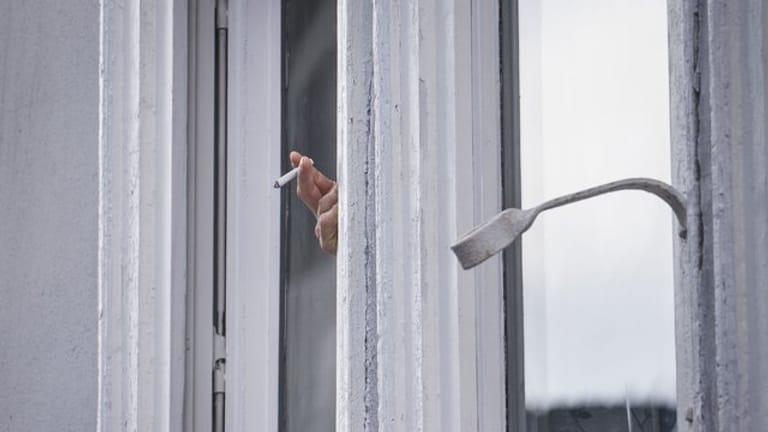 Ein Mann raucht während der Ausgangsbeschränkung am Fenster.