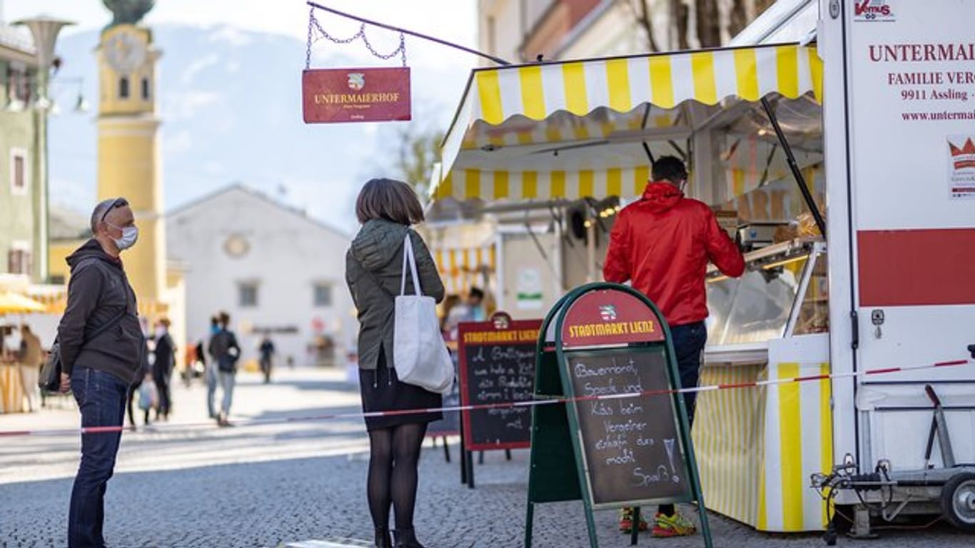Menschen mit Mundschutz stehen an einem Marktstand in Lienz im Tirol an.