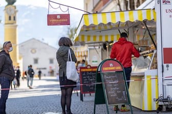 Menschen mit Mundschutz stehen an einem Marktstand in Lienz im Tirol an.