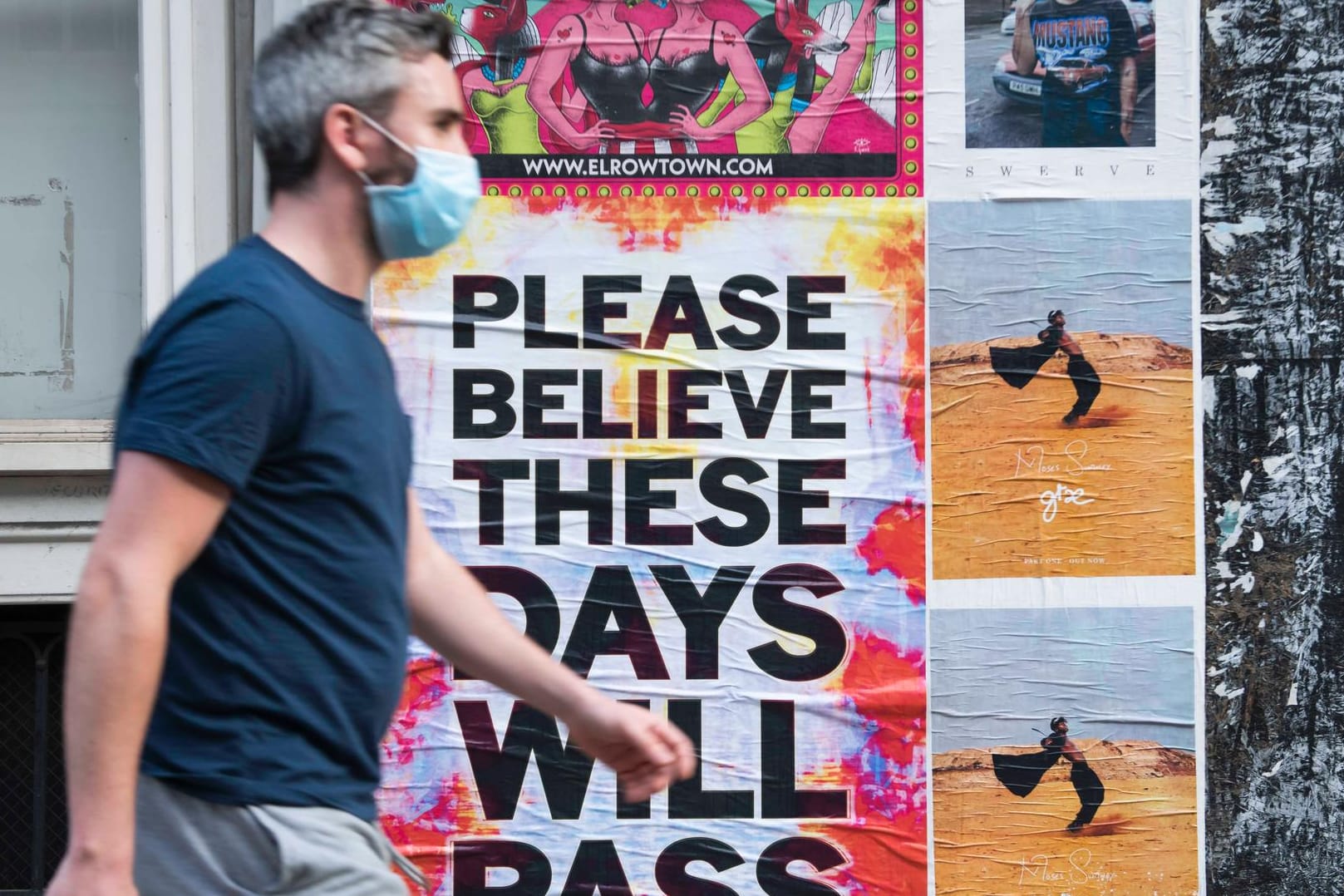 Zeichen der Corona-Krise: In London gehören Schutzmasken zum Alltag. Im Hintergrund ein motivierendes Plakat: "Bitte glaube daran, dass diese Tage vorbeigehen".