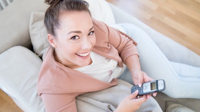 Eine Frau mit Telefon in der Hand (Symbolbild): Damit Verbraucher nach dem Anbieterwechsel weiter unter der alten Rufnummer erreichbar sind, sollten sie diese portieren lassen.