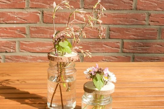 Ein altes Glas als Vase ist nichts Besonderes - mit einer durchlöcherten Holzscheibe bekommt das Ganze aber etwas Besonderes.