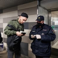 Ein Polizeibeamter mit Schutzmaske kontrolliert die Papiere eines Passanten am Eingang der Moskauer Metro.