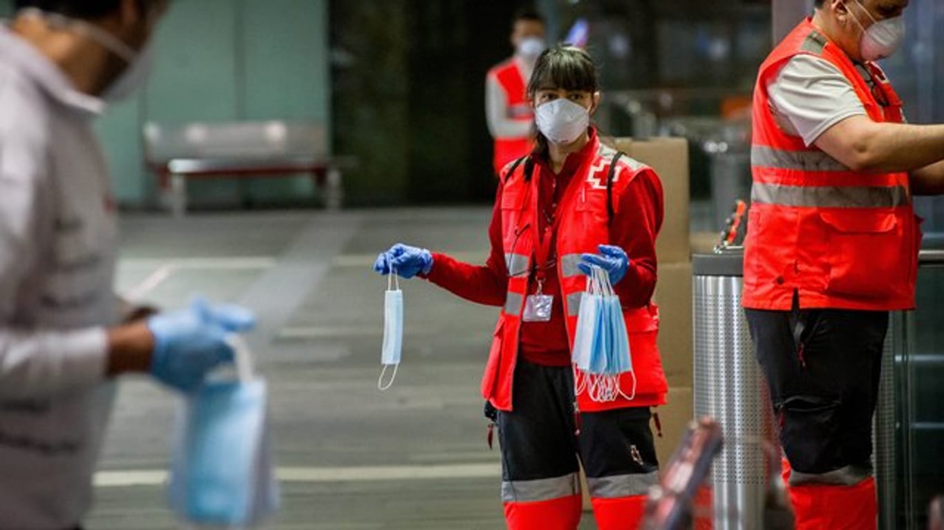 Freiwillige Mitarbeiter des Roten Kreuzes verteilen vor dem Bahnhof Barcelona-Catalunya Mundschutzmasken an Passagiere.