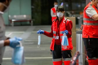 Freiwillige Mitarbeiter des Roten Kreuzes verteilen vor dem Bahnhof Barcelona-Catalunya Mundschutzmasken an Passagiere.