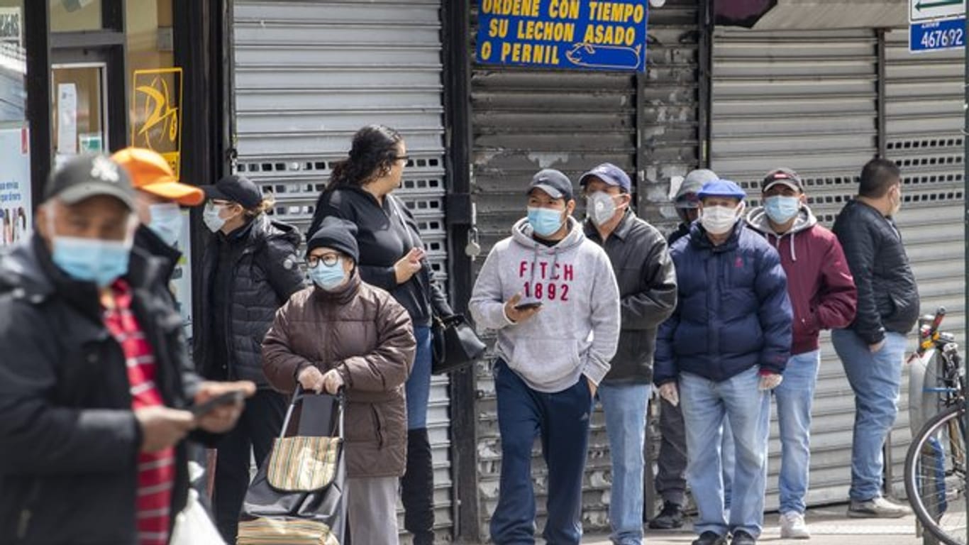 Menschen mit Mundschutz stehen in einer Schlange vor einem Lebensmittelgeschäft im New Yorker Stadtteil Queens.