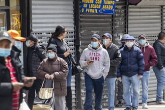 Menschen mit Mundschutz stehen in einer Schlange vor einem Lebensmittelgeschäft im New Yorker Stadtteil Queens.