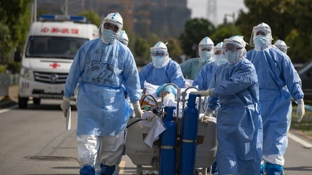 Medizinisches Personal in Schutzanzügen schiebt in Wuhan einen Covid-19-Patienten über eine Straße, um ihn in die Intensivstation zu verlegen. Medizinisches Personal in Schutzanzügen schiebt in Wuhan einen Covid-19-Patienten über eine Straße, um ihn in die Intensivstation zu verlegen.