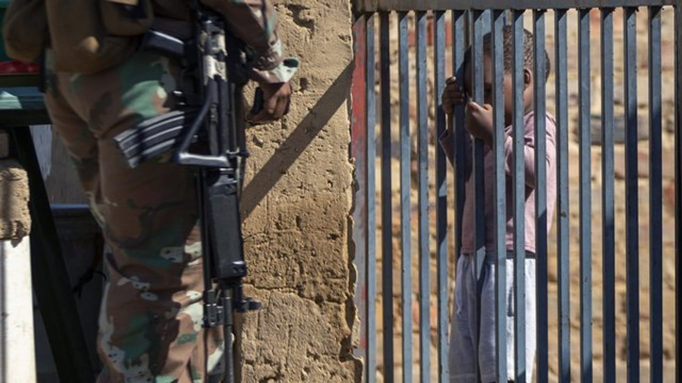 Ein Kind hält sich im südafrikanischen Johannesburg an einem Torgitter fest, hinter dem ein Mitglied der Nationalen Verteidigungskräfte steht.