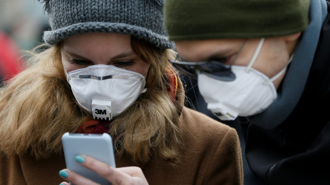 Menschen mit Schutzmasken und Smartphone (Symbolbild): Eine Corona-Warn-App soll in Deutschland erst im Mai erscheinen.