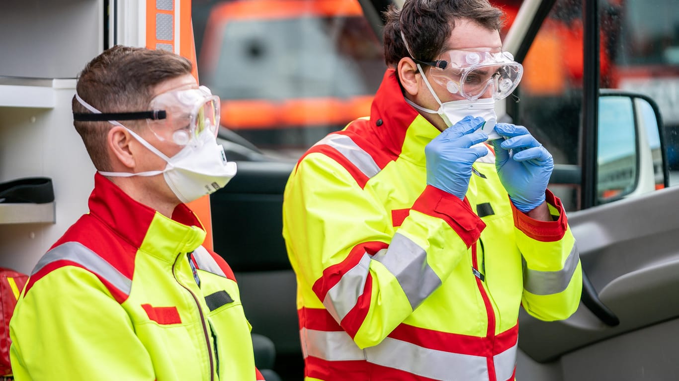 Mitarbeiter der Kölner Feuerwehr zeigen ihre Schutzausrüstung (Archivbild): Auch Notfallsanitäter, Rettungssanitäter und Rettungsassistenten haben mit den Auswirkungen des Coronavirus zu kämpfen.