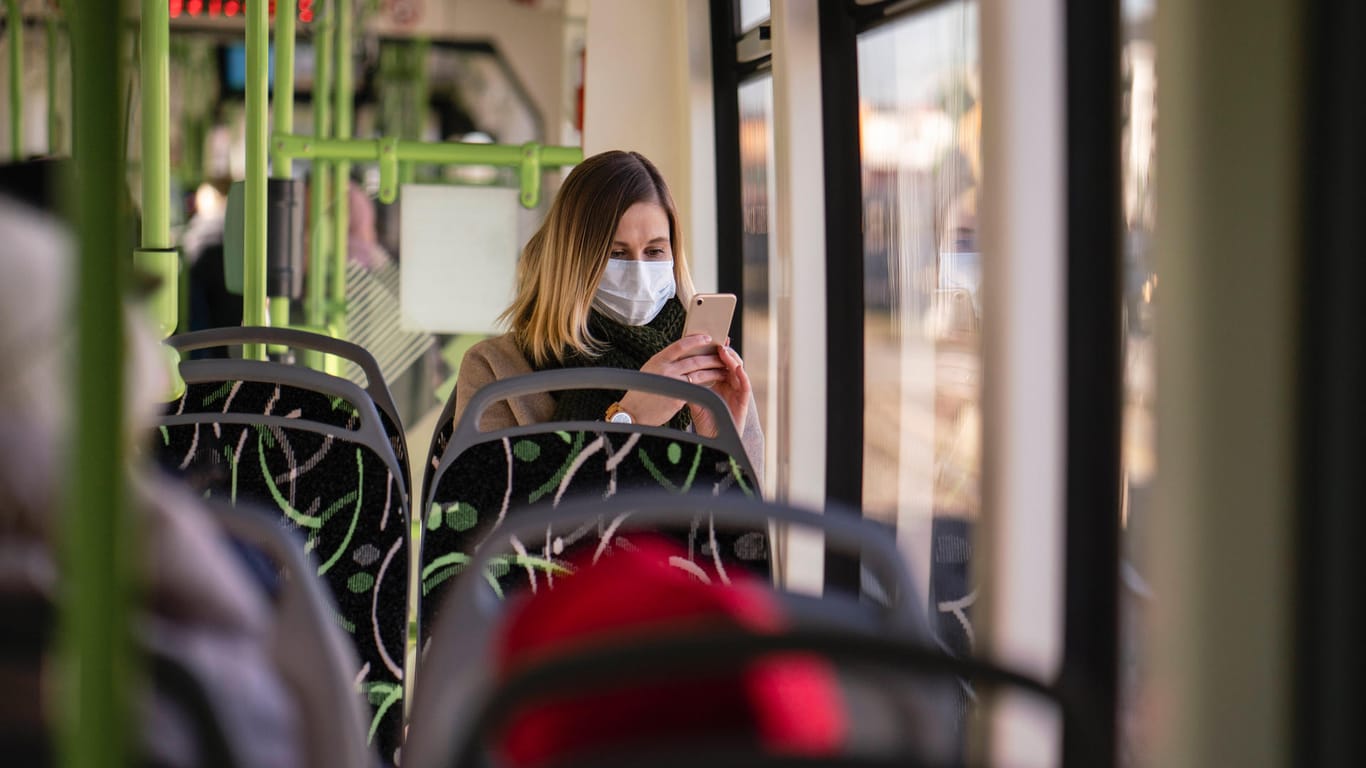 Eine Frau mit Maske in der Straßenbahn: Forscher streiten sich um Datenschutz bei Corona-Warn-Apps.