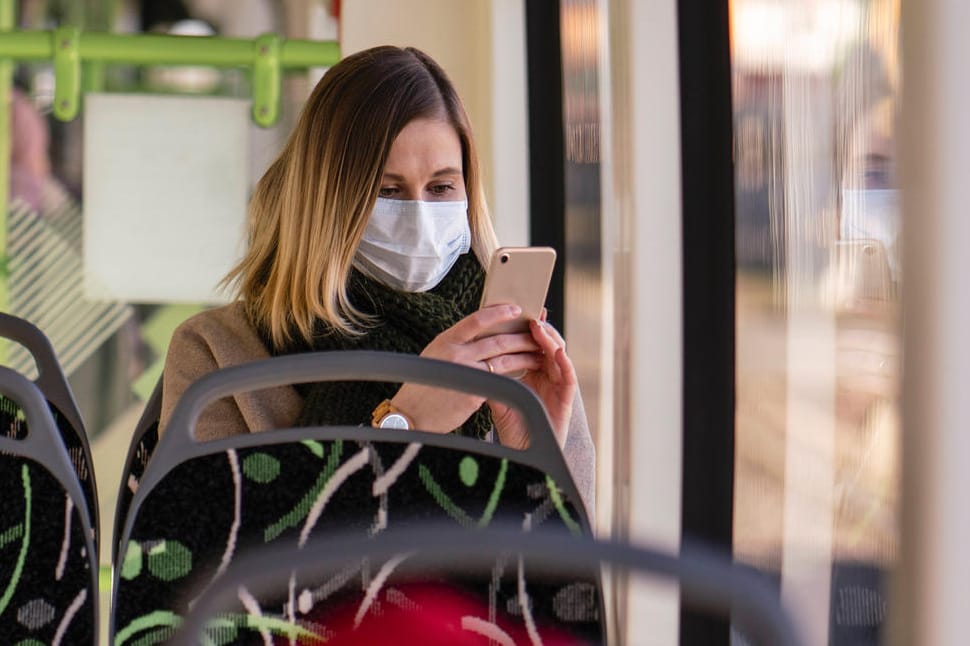 Eine Frau mit Maske in der Straßenbahn: Forscher streiten sich um Datenschutz bei Corona-Warn-Apps.