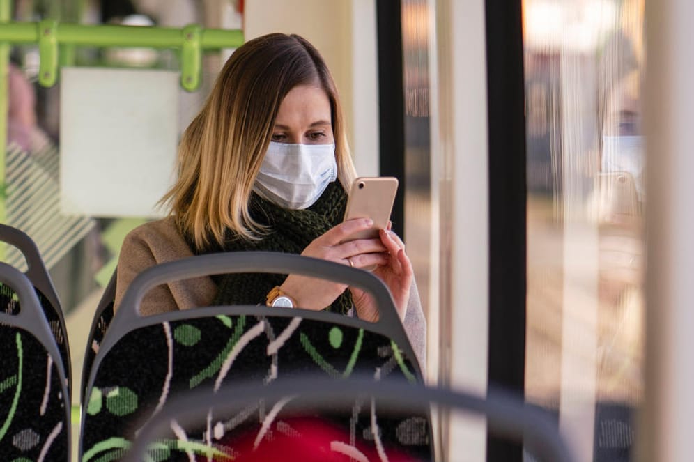 Eine Frau mit Maske in der Straßenbahn: Forscher streiten sich um Datenschutz bei Corona-Warn-Apps.