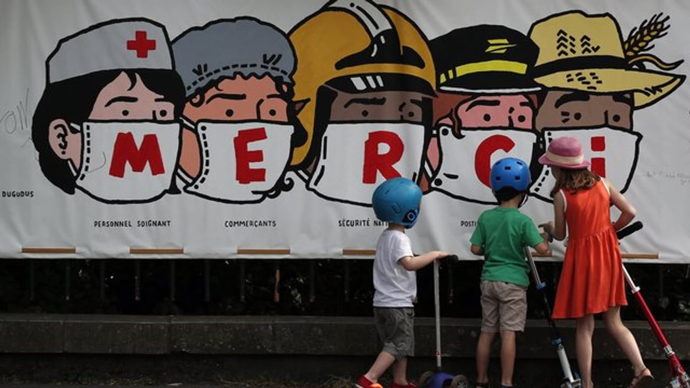 Kinder in Paris betrachten ein Banner, auf dem eine Danksagung an verschiedene systemrelevante Berufsgruppen aufgedruckt ist.