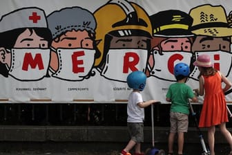 Kinder in Paris betrachten ein Banner, auf dem eine Danksagung an verschiedene systemrelevante Berufsgruppen aufgedruckt ist.