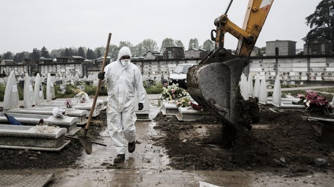 Ein Mitarbeiter im Schutzanzug geht in der Industriestadt Turin über einen Friedhof, auf dem frische Gräber ausgehoben werden.