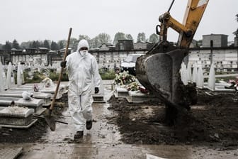Ein Mitarbeiter im Schutzanzug geht in der Industriestadt Turin über einen Friedhof, auf dem frische Gräber ausgehoben werden.