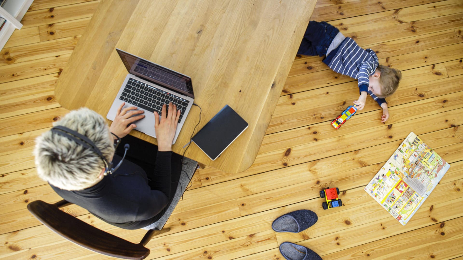 Eine Frau arbeitet im Homeoffice, während ihr Kind unter dem Tisch spielt (Symbolfoto): Viele Eltern müssen ihre Kinder derzeit zu Hause betreuen.