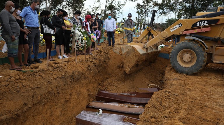 Massengrab für Covid-19-Opfer: Ein Radlader schiebt Sand in eine Grube, in der mehrere Särge aufgereit sind.