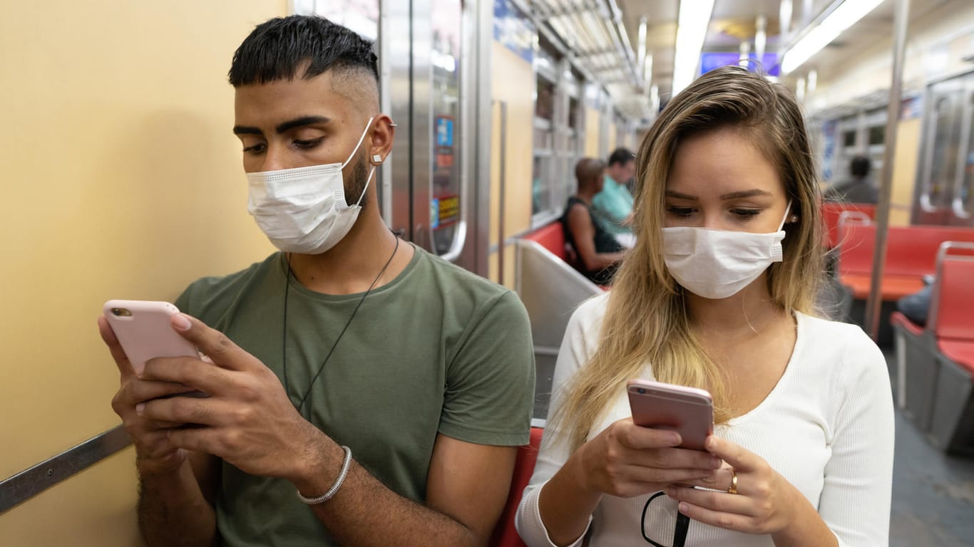 Menschen mit Maske und Smartphone (Symbolbild): Derzeit für über ein Konzept für eine Corona-Warn-App diskutiert.