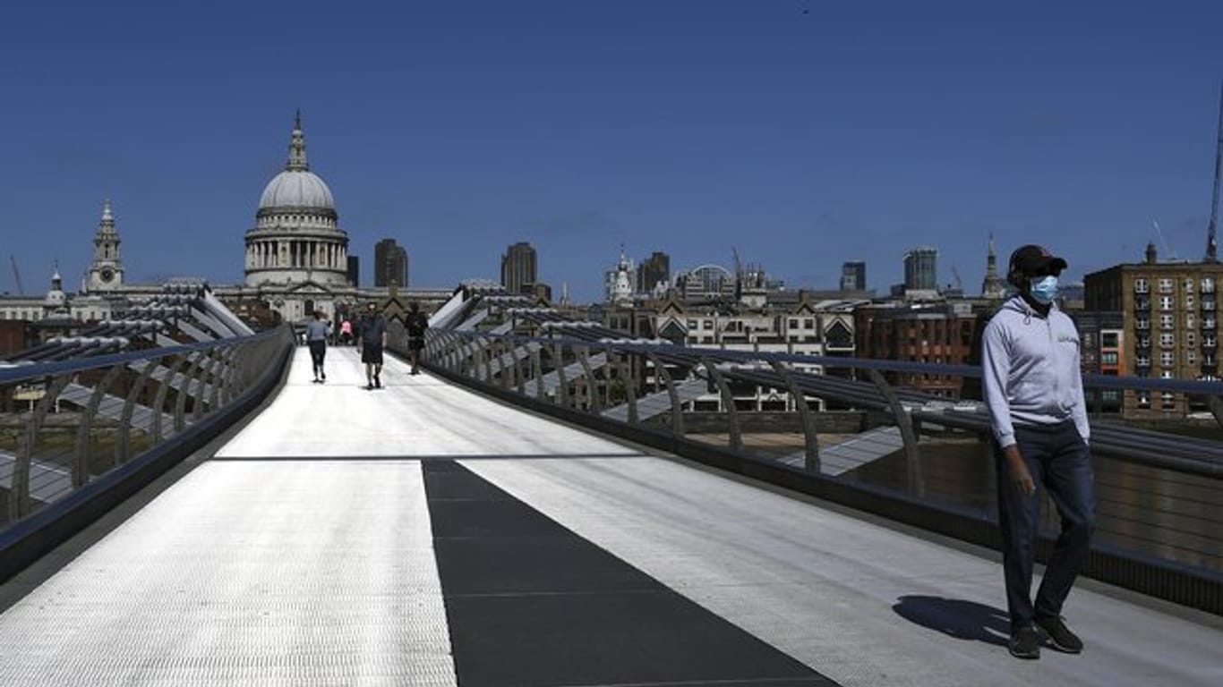 Ein Mann mit Mundschutz überquert während der anhaltenden Ausgangsbeschränkungen die fast menschenleere Millennium Bridge in London.