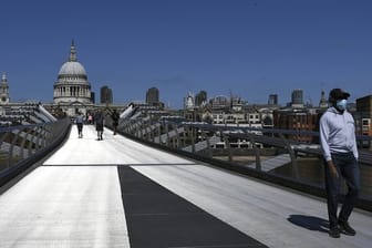 Ein Mann mit Mundschutz überquert während der anhaltenden Ausgangsbeschränkungen die fast menschenleere Millennium Bridge in London.