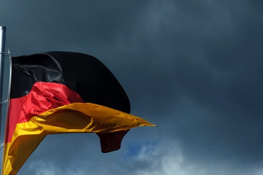 Eine Deutschlandfahne vor dunklen Wolken.