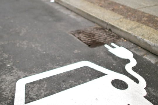 Ein Elektrofahrzeug kennzeichnet einen Parkplatz neben einer Ladesäule an einer Straße.