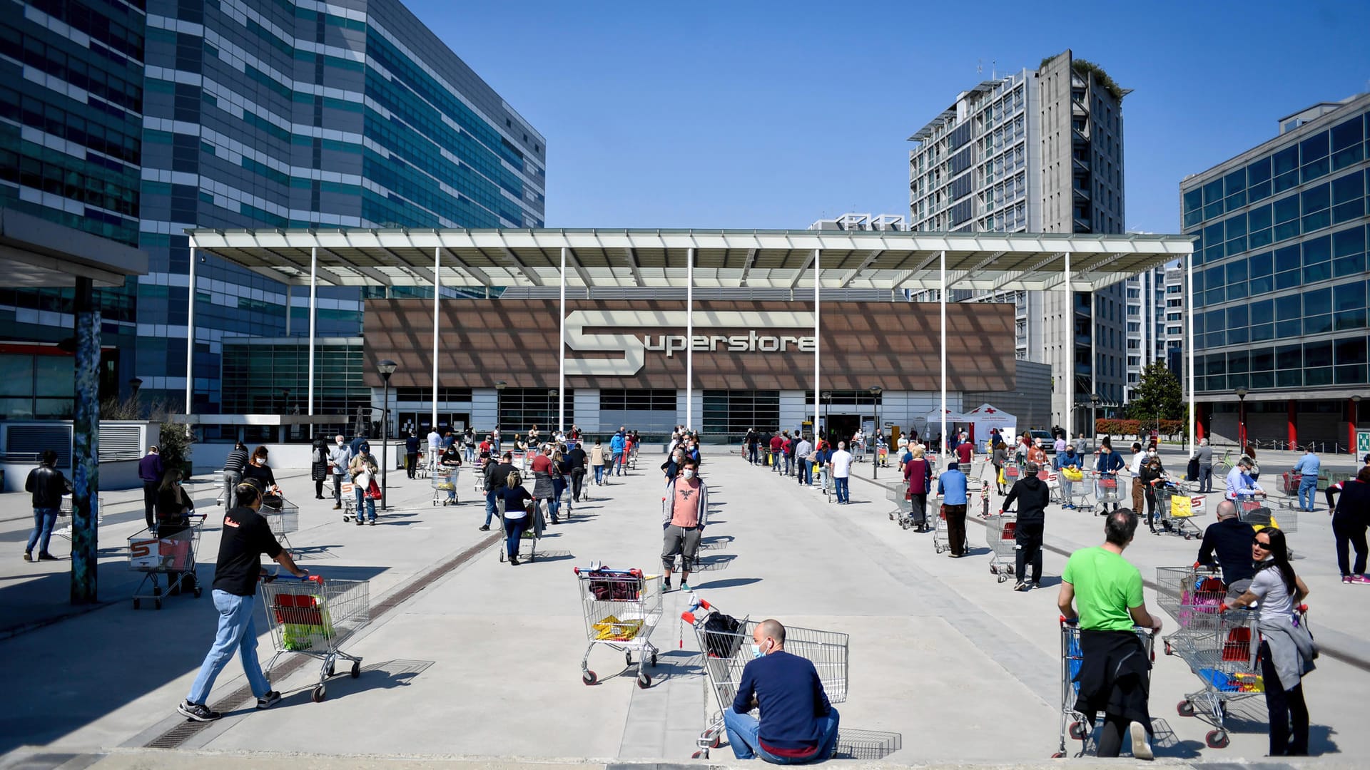 Menschen stehen mit ihren Einkaufswagen vor einem Supermarkt in Mailand Schlange: Die Corona-Regelungen in Italien sind strikter als die deutschen Schutzmaßnahmen. (Archivbild)