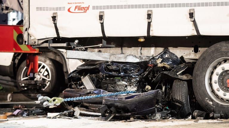 Ein völlig zerstörtes Auto liegt quer unter einem LKW Anhänger: Drei Menschen sind bei einem Zusammenstoß mehrerer Fahrzeuge auf einem Autobahnparkplatz im Ruhrgebiet ums Leben gekommen.