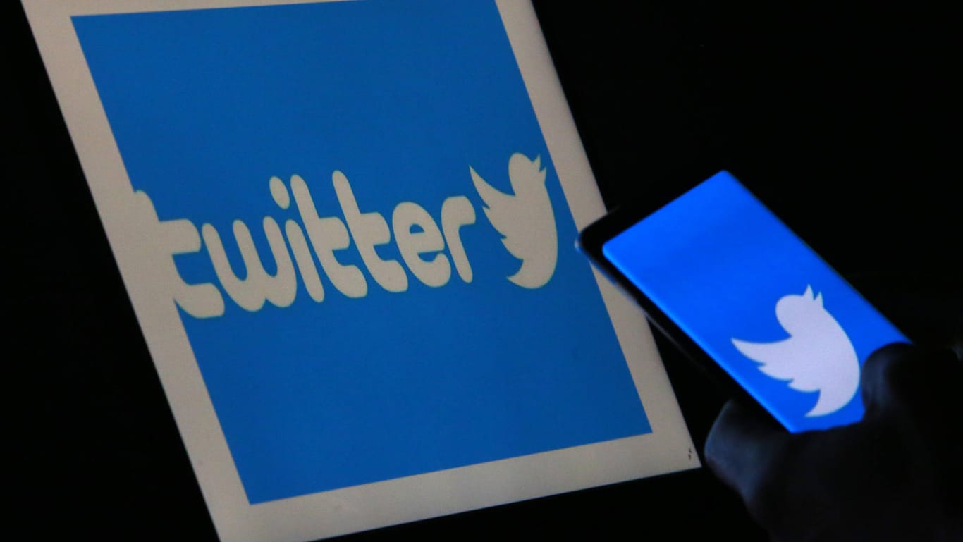Eine Hand hält ein Handy vor dem Twitter-Logo: Beiträge auf der Plattform können zum Teil eine große Reichweite erreichen.
