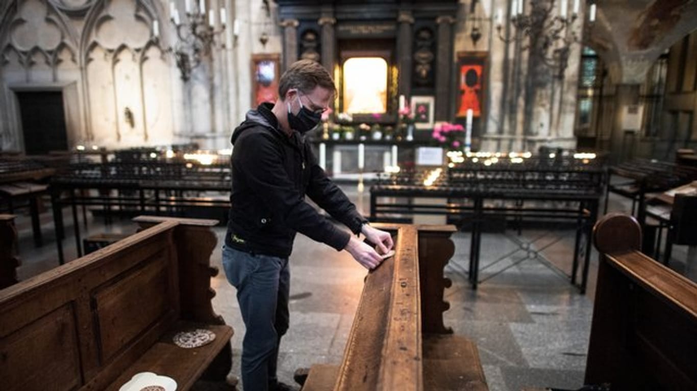 Ein Mitarbeiter der Dombauhütte klebt Aufkleber auf Kirchenbänke im Kölner Dom.