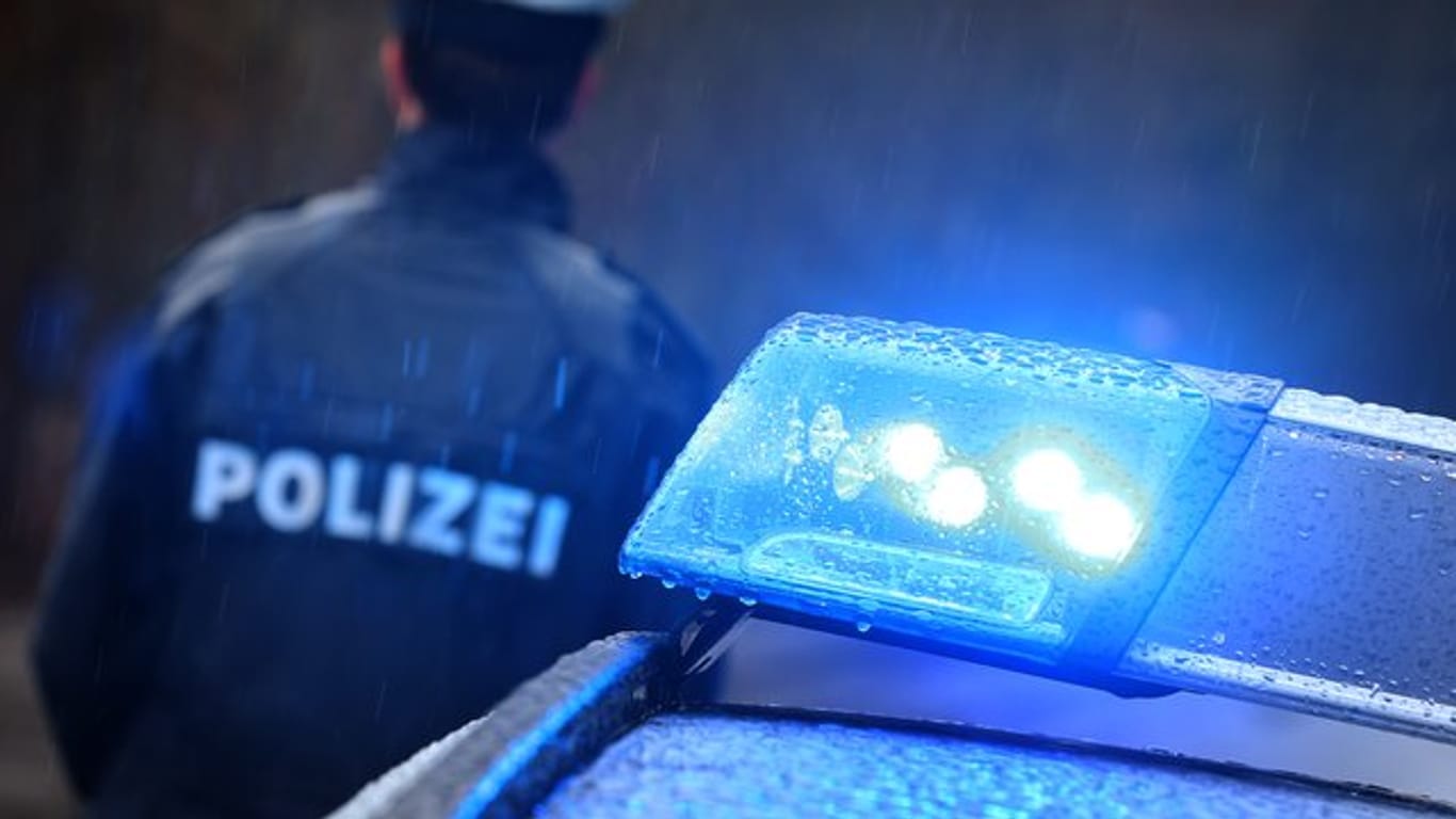 Ein Polizist steht im Regen vor einem Streifenwagen