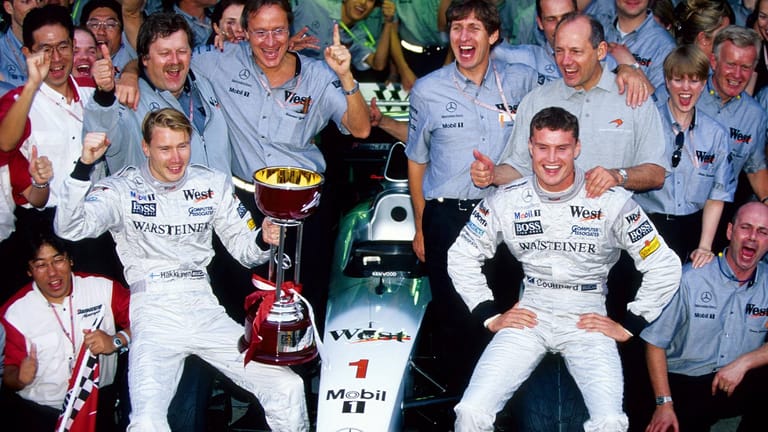 Höhepunkt: Häkkinen (li.) feiert mit Teamkollege David Coulthard (r.) und dem Team von McLaren Mercedes seinen ersten WM-Titel 1998.