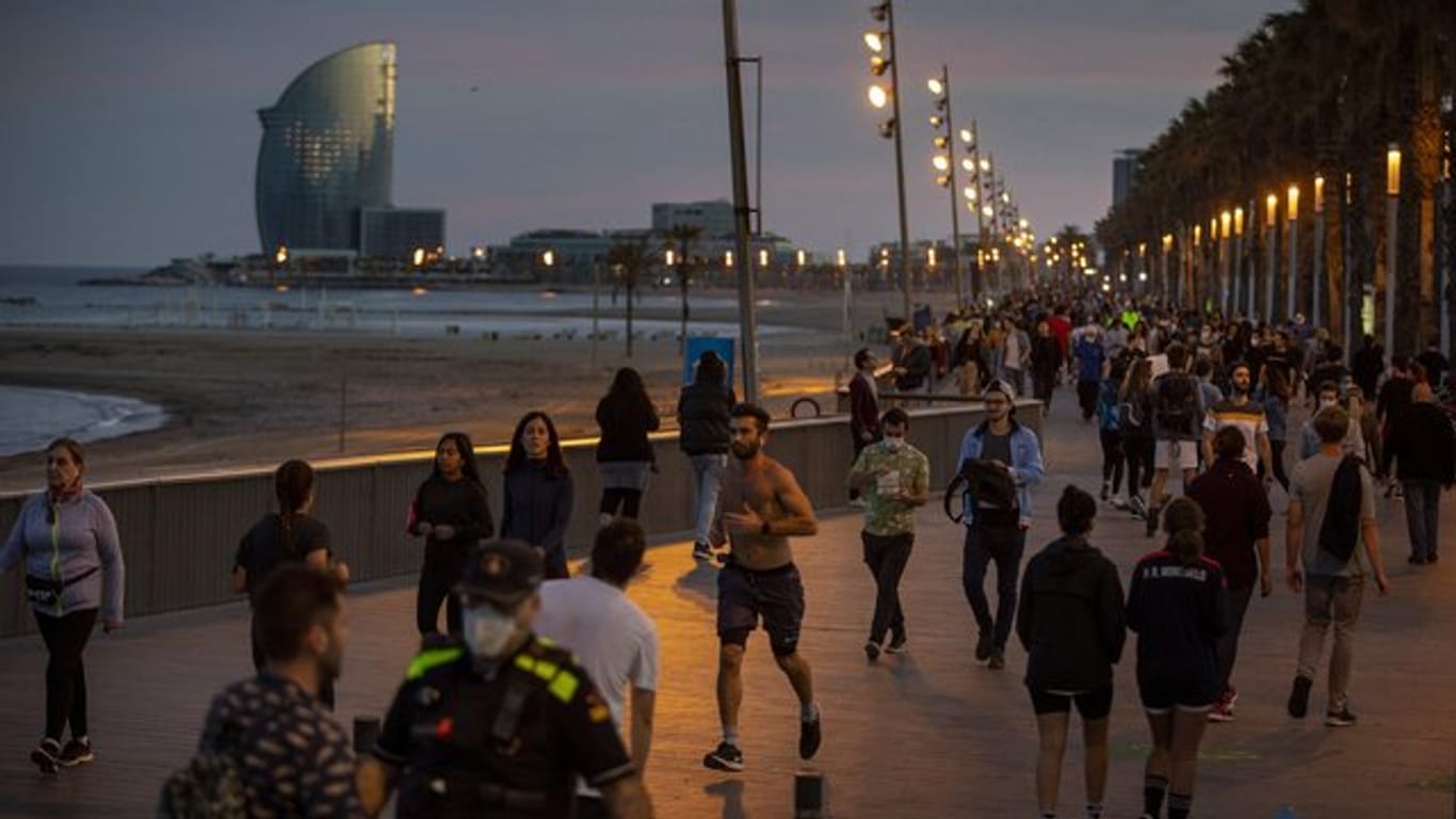Menschen gehen bei Sonnenuntergang auf einer Strandpromenade spazieren und treiben Sport.