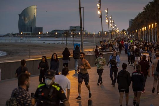 Menschen gehen bei Sonnenuntergang auf einer Strandpromenade spazieren und treiben Sport.