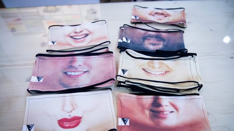 Fotomasken als Mund-Nase-Schutz liegen auf einem Tisch: Welches Lächeln darf es sein?